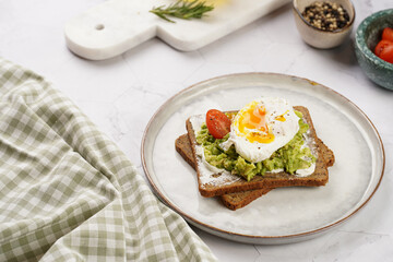 Trendy lifestyle sandwich: protein bread slice with cream cheese, mashed avocado, cherry tomatoes and poached egg on white scandi plate, light setting