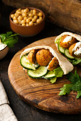 Traditional oriental chickpea deep fried falafel in flatbread pita, tzatziki yoghurt sauce, hummus, fresh lime and green cilantro on wooden board, dark surface
