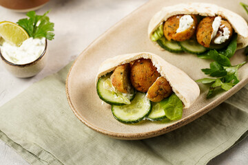 Traditional oriental chickpea deep fried falafel in flatbread pita, tzatziki yoghurt sauce, hummus, fresh lime and green cilantro on light surface