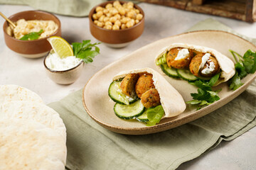 Traditional oriental chickpea deep fried falafel in flatbread pita, tzatziki yoghurt sauce, hummus, fresh lime and green cilantro on light surface