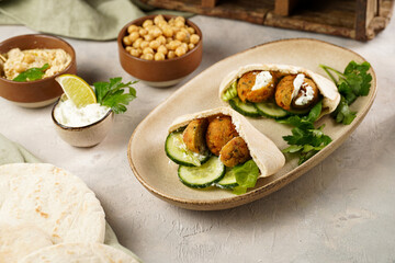 Traditional oriental chickpea deep fried falafel in flatbread pita, tzatziki yoghurt sauce, hummus, fresh lime and green cilantro on light surface