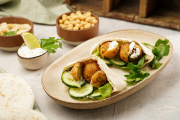 Traditional oriental chickpea deep fried falafel in flatbread pita, tzatziki yoghurt sauce, hummus, fresh lime and green cilantro on light surface