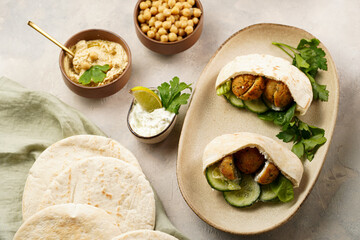 Traditional oriental chickpea deep fried falafel in flatbread pita, tzatziki yoghurt sauce, hummus, fresh lime and green cilantro on light surface