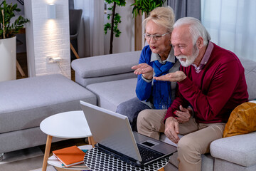 Lovely senior couple is sitting on a sofa and talking to their children and grandchildren via video...