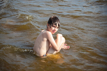 Smiling boy sitting in water with wet hair on sunny day