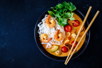 Tom Yum - Thai soup with prawns and rice noodles on black wooden table
