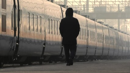 A man in black clothes walks alone along the platform of the railway station against the background of a moving train.