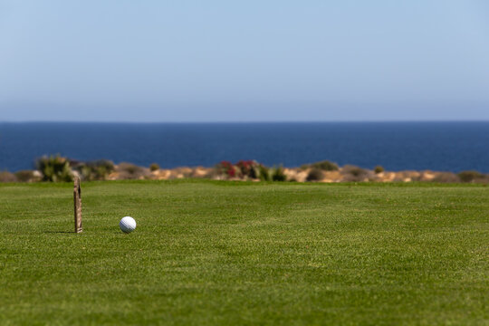 Tropical seaside golf course. Close-up view of golf ball on tee box with deep blue ocean and clear blue sky in background. Copy space.