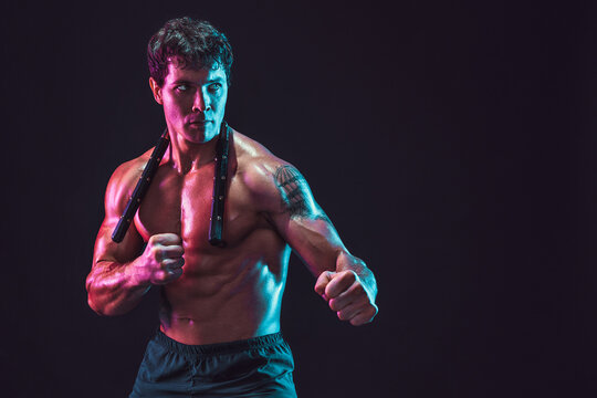 Half length of strong male athlete who poses with nunchaku on black background. Sport concept 