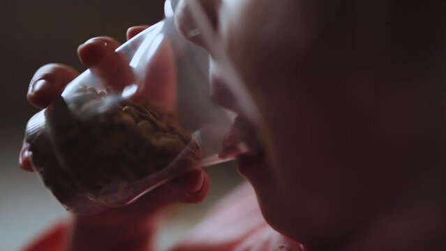 A little girl of 4 years old eats peeled sunflower seeds from a plastic cup