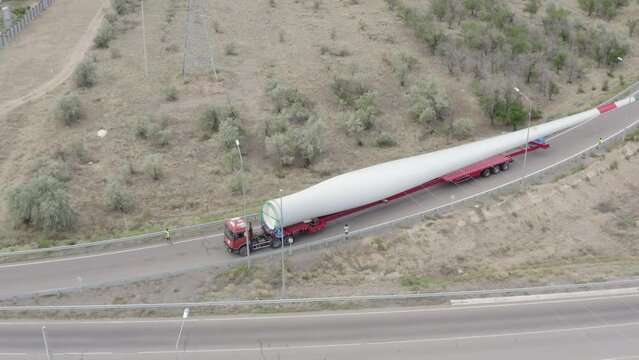 Aerial footage of a huge truck loaded with a blade of a wind turbine rides along the roundabout