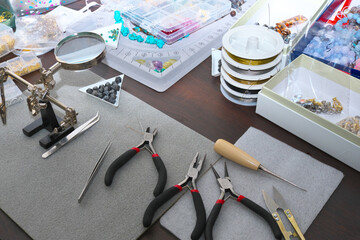 Composition of jewelry making supplies, colorful shiny mixed beads, pliers and craft wire on a gray fabric background, close up. Selective focus.