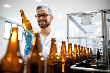 Beverage bottling factory and technologist worker checking beer bottles before filling with alcohol...