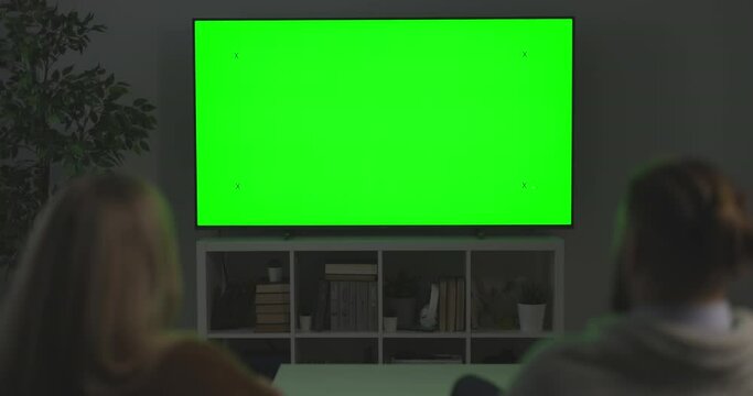 Caucasian man and woman discussing something while sitting on sofa and looking on TV with chroma key screen. Back view, copy space.