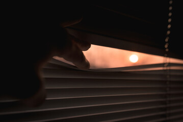 peeking at sunset behind a venetian blind. winter sun in the window at sunset