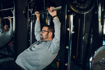 Middle aged man lifting barbell while training in the gym