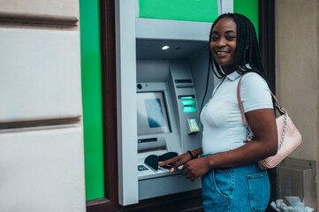 Cheerful african american woman using credit card and an atm machine