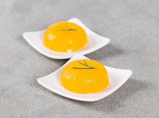 Tangerine jelly in the shape of a small hemisphere on a plate on a light gray background