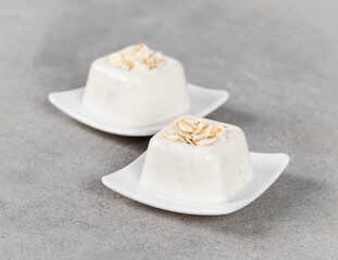 Oatmeal cream dessert in the shape of a French square savarin on a plate on a light gray background