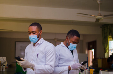 two handsome african doctors in the clinic surfing the internet with there cellphone