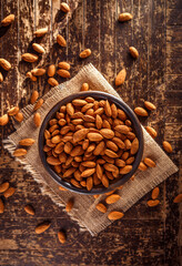 Overhead view of a bowl of raw whole organic almonds on a rustic wooden surface