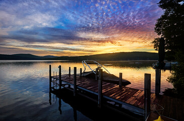 Minutes before sunrise, clouds light up with pinks and yellows over a New Hampshire lake