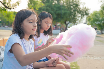 Adorable little sisters eating candy-floss outdoors at summer