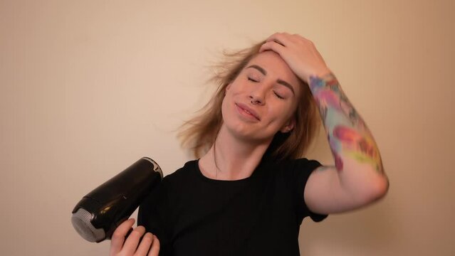 Girl in a good mood dries her hair with a hairdryer and smiles