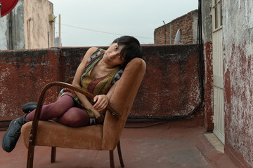 Mujer mexicana sentada en silla mirando de lado en azotea de edificio viejo