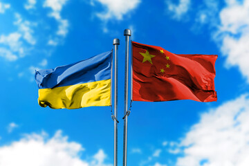 Flags of Ukraine and China on the wind against blue sky