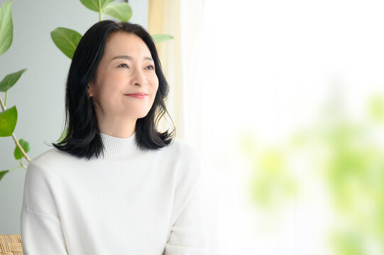 逆光の明るい窓際で微笑む美しい日本人（アジア人）女性　右にコピースペースあり　前ボケ　	