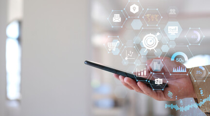 Businessman uses his smartphone to analyze sales data and an economic graph chart in order to...