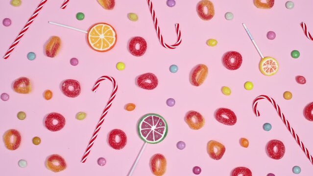 Patel pink background full with moving candies, lollypops and gummy candies. stop motion animation flat lay pattern