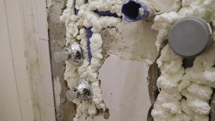 A close up shot of shower fittings and new plumbing pipes of a section of a bathroom currently undergoing maintenance, all the pipes are well insulated with expanding spray foam