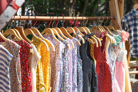 Wooden clothes racks with hangers and with colorful dresses. Showcase with clothes on street market.