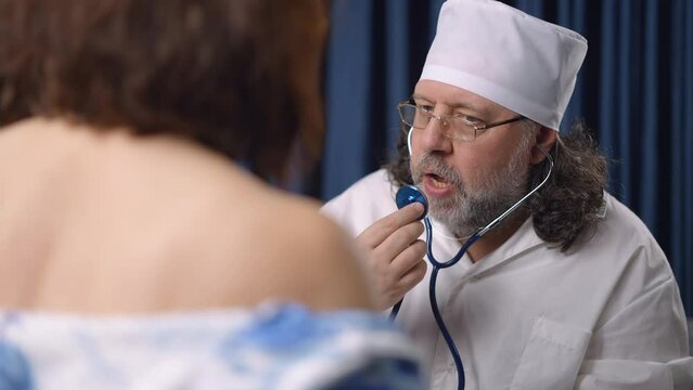 The doctor uses a stethoscope to listen to the patient's lungs and heart. The therapist examines and diagnoses the female patient. Detection of the disease in a medical institution. City hospital.