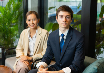 Young businessman and businesswoman working together, sitting, looking at camera, focus at man. Young man and woman work business in hotel cafe