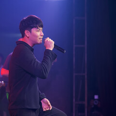Young black-haired asian singer with a microphone singing on stage. The atmosphere at night in the...