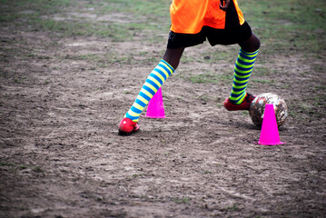Footballer dribbling ball during training between cones. Young soccer players practicing dribbling.