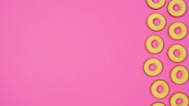 Round cookies in two columns move on right side of vibrant pink theme. Stop motion flat lay
