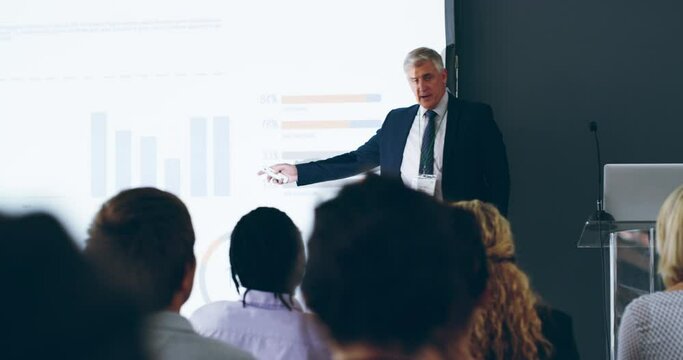 Presentation skills that make an impact. Mature businessman mentor and coach pointing at a screen in a presentation at a conference in a modern office. Ceo, boss or manager giving training at workshop