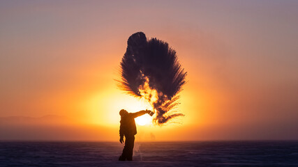 Man on a frozen lake at sunrise. in arctic Canada. Person splashes boiling water on cold air which instantly turns to snow, steam in freezing temperatures. 
