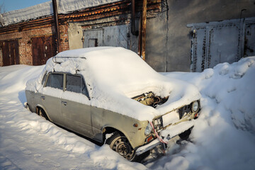 Snowdrift on an abandoned old car in industrial zone. Winter. Season specific. Outdoors