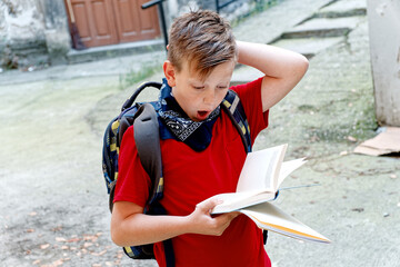A boy, an elementary school student, surprised by what he's reading in a book, making an expression of shock and awe