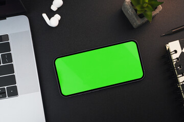 Smartphone with green screen on black background table. Office environment. Chroma Key