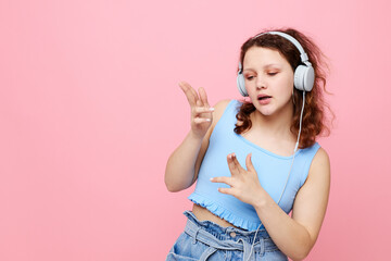 Fototapeta premium portrait of a young girl in headphones listening to music on a pink background unaltered