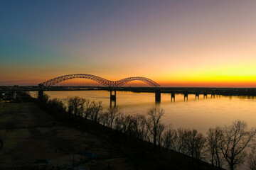 Fototapeta na wymiar a stunning aerial shot of a long metal bridge over the Mississippi river at sunset with a gorgeous blue, yellow and orange sky and lights on the bridge at Mud Island in Memphis Tennessee USA