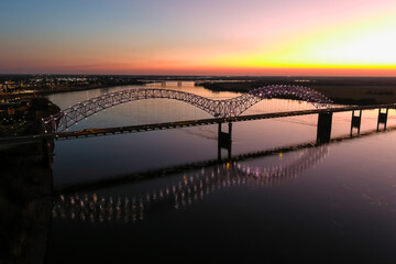 a stunning aerial shot of a long metal bridge over the Mississippi river at sunset with a gorgeous blue, yellow and orange sky and lights on the bridge at Mud Island in Memphis Tennessee USA