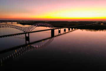 a stunning aerial shot of a long metal bridge over the Mississippi river at sunset with a gorgeous...