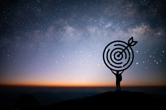 Silhouette of young businessmen hold target on top of a mountain at night with star and Milky Way over the sky. Shows the goal setting.